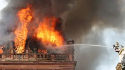 PA A firefighters hoses the fire at the Primark store in Belfast