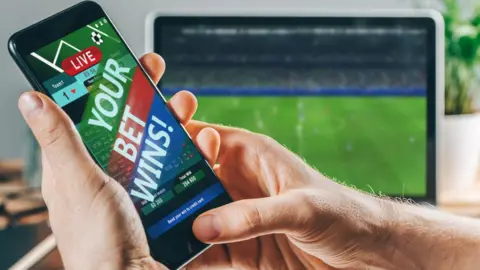 Getty Images Phone with winning of a bet in front of football on a screen