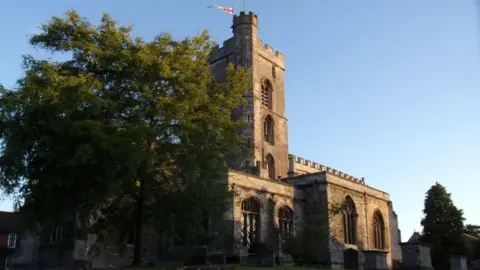 All Saints Church A church building at dusk with a setting sun casting light onto the building.