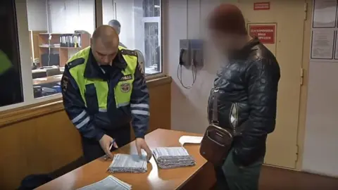 Moscow police Driver standing next to a desk with three stacks of paper on it