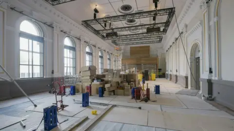 Bristol Beacon A room with large arched windows and theatre lighting going through renovation.