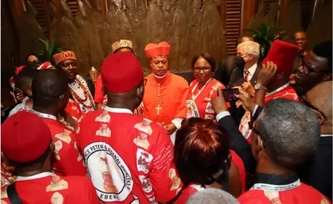 Getty Images Cardinal Peter Ebere Okpaleke wearing cardinal clothes, and a sea of people all around him also dressed in red. One person is taking a picture.