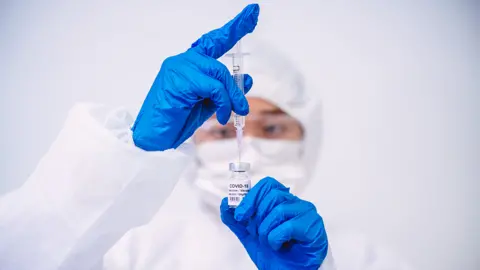 Getty Images Scientist with syringe and bottle marked "Covid 19"