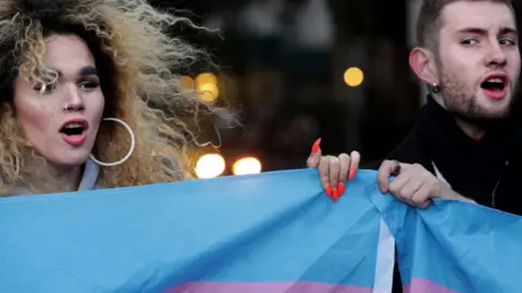 Getty Images Two protesters hold up a flag for Transgender and Gender Non-comforming people