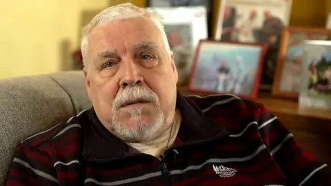 BBC a grey-haired man looks down the camera