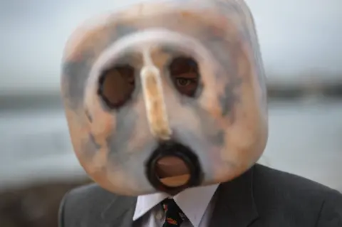 Rodger Bosch/AFP Man with a plastic mask on and a dark suit - 5 June.