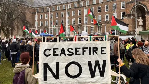 A protest in front of Bristol civic offices with a large 'Ceasefire Now' banner and Palestinian flags