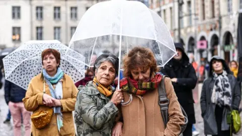 EPA People gather to watch the funeral ceremony of French teacher Dominique Bernard on a screen in Place des Heros in Arras, 19 October 2023.