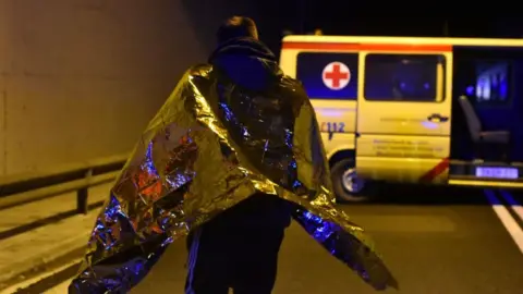 EPA A man wearing a silver blanket stands near the ambulance