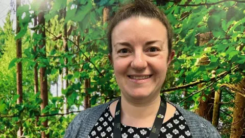 ANDREW TURNER/BBC Deputy headteacher Laura Brett stands in front of woodland scene