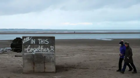 PA Media A man and a woman walk along a beach in Dublin where the words "Still in this together" have been painted on a concrete slab