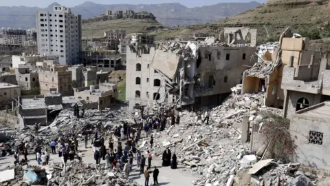 EPA Yemenis stand amid the remains of a block of flats destroyed in an air strike in Sanaa, Yemen (26 August 2017)