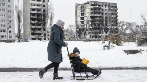 Getty Images A woman carries the child after the snowfall as daily life continues in Borodianka