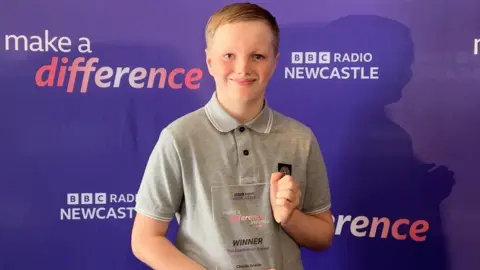 A young boy, Charlie Graver, holds a glass award