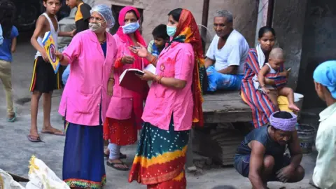 Getty Images Asha health workers talk amongst themselves while conducting door to door survey to identify Covid-19 cases as JJ colony in Patparganj has already reported above 70,000 cases, near Mayur Vihar on June 25, 2020 in New Delhi, India