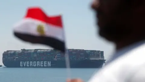 Reuters A man holds an Egyptian flag as Ever Given is seen at the Suez Canal in Egypt"s Great Bitter Lake in Ismailia, Egypt, July 7, 2021