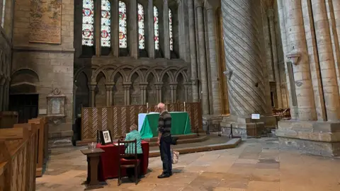 A woman signs the book of condolence while a man watches