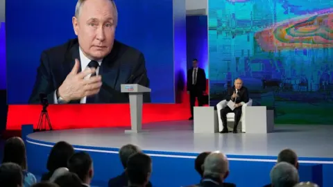 EPA Vladimir Putin sits on stage at election headquarters in Moscow, Russian Federation with a big screen behind him showing his face on 31 Jan 2024