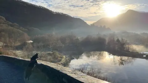 Llyn Padarn at Llanberis, looking towards Snowdon with sun over the peak, and a border collie dog looking over the lake from a viewpoint