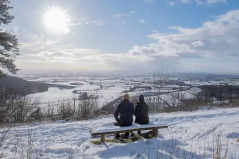 AFP A couple sit on a bench overlooking the snow-covered fields of Thirsk at Sutton bank National Park Centre in the North Yorks Moors National Park in North Yorkshire