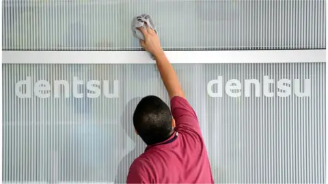 AFP A man cleans a logo on a wall for Japan's Dentsu advertising agency