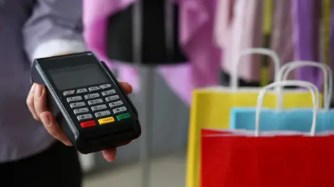 Getty Images/Ivan-balvan Shop worker holds out chip and PIN payment card reader