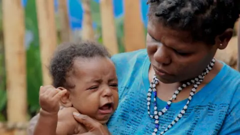 BBC News Indonesia/Oki Budhi Jubiana Kogeya holding her baby, who is crying