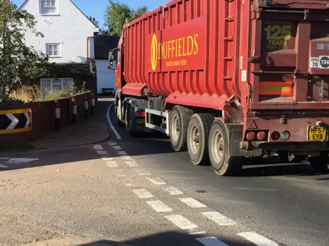 BBC HGV lorry driving through village on single carriageway of A12