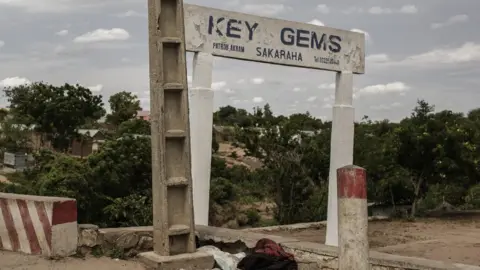People cross a bridge as a a gems and precious stones seller advertising sign post is seen in the mining town of Sakaraha