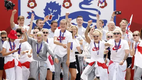 PA Media The England women's football team celebrate their Euros victory at London's Trafalgar Square in front of an England football icon