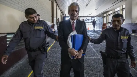 EPA-EFE/REX/Shutterstock Handcuffed José Zamora (centre) is escorted by police officers to a court hearing in Guatemala City, Guatemala. Photo: 14 June 2023