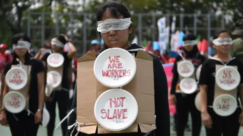 Getty Images Migrant workers are seen wearing blindfolds and wearing cardboard signs during the May Day rally in Hong Kong