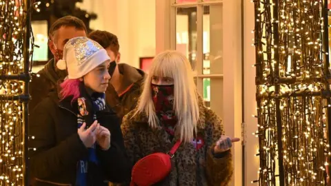 Getty Images Shoppers wearing face coverings to combat the spread of Covid-19, leave through the decorations adorning a doorway of a store in central London on December 21, 2021