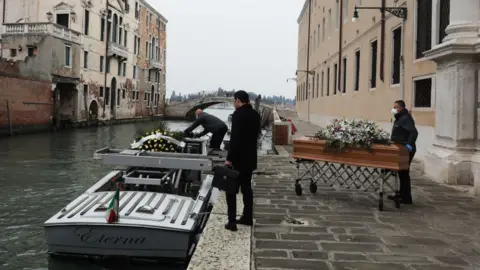 Getty Images Undertakers place coffins on a boat in Venice