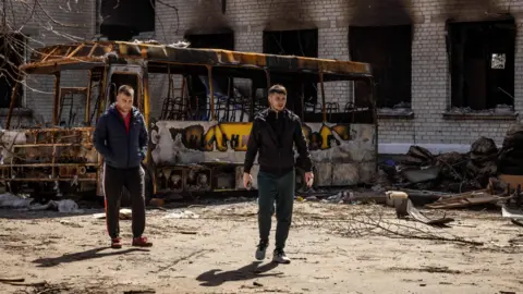 Men walk near a burnt bus and a damaged school in Bohdanivka village