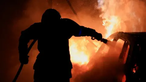 Pascal Rossignol / Reuters A French firefighter works to extinguish a burning car in Tourcoing, France