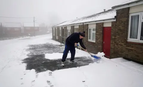 PA/Owen Humphreys A man clears snow from the drive of his home in Tow Law, County Durham.
