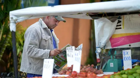 A fruit vendor reads a newspaper in the streets of San Jose