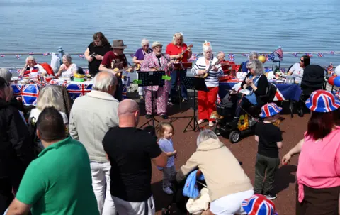 Reuters People watch Morecambe Ukulele Club play some music during celebrations for the Big Lunch on the prom, in Morecambe, Britain, May 7, 2023