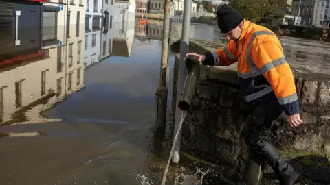 CLODAGH KILCOYNE/REUTERS Man empties floodwater out of his boot in Newry