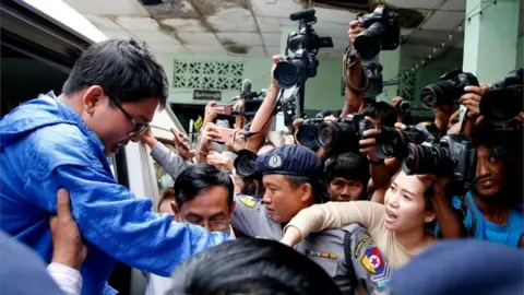 Reuters Reuters reporter Wa Lone's wife Pan Ei Mon (2nd-R) tries to catch his hand as he arrives at court in Yangon, Myanmar, 27 December 27, 2017.