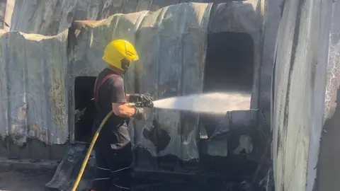 Cambridgeshire Fire and Rescue Service Fire-fighter uses hose to dampen hotspots at Corkers Crisps