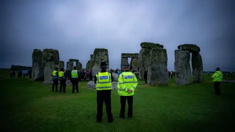 PA Media Police watch crowds celebrate during Summer Solstice at Stonehenge, where some people jumped over the fence to enter the stone-circle to watch the sun rise at dawn of the longest day in the UK.