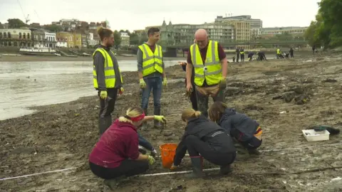 Volunteers pull wet wipes out of the river bank