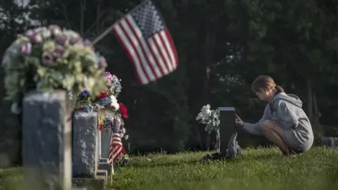 BBC A woman mourns at a gravestone in Austin, Indiana