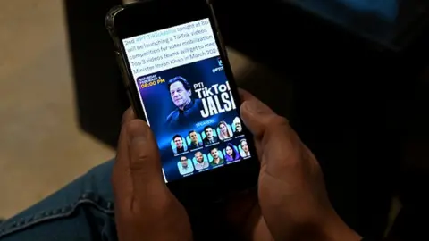 Getty Images Pakistan's former prime minister Imran Khan's supporter listens to a virtual election campaign on a phone