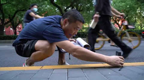 Mr Deng measures the length of the road with a rangefinder.