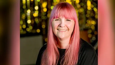 Sybil Bell Sybil Bell, who has pink hair,smiling with lights in the background