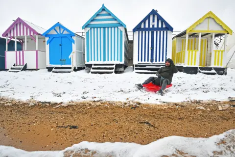 PA Media A man sits on a sledge on the snow-covered beach at Thorpe Bay, Essex, on 9 February 2021