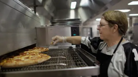 Getty Images Woman checks the temperature of a pizza during school lunch service